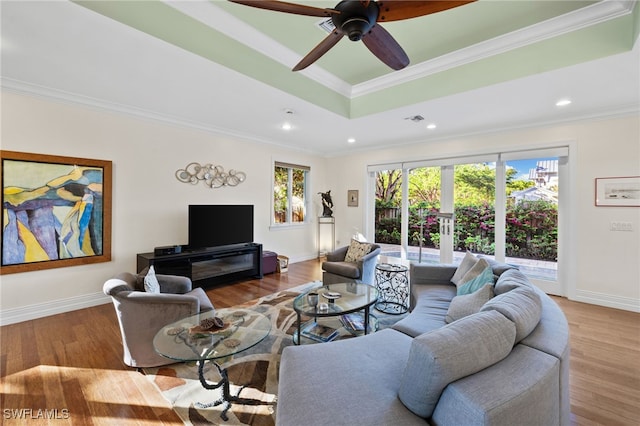 living room with ceiling fan, light wood-type flooring, ornamental molding, and a tray ceiling