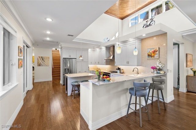 kitchen featuring kitchen peninsula, wall chimney exhaust hood, a breakfast bar, white cabinets, and hanging light fixtures