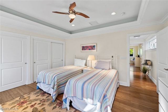 bedroom with dark wood-type flooring, baseboards, ornamental molding, a closet, and a raised ceiling