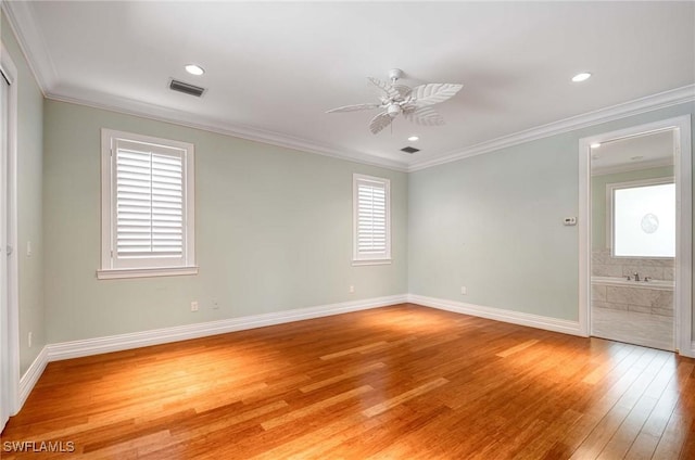 spare room with light wood finished floors, baseboards, visible vents, a ceiling fan, and ornamental molding