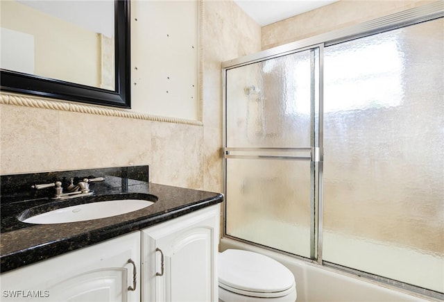 full bathroom with vanity, toilet, bath / shower combo with glass door, and tile walls