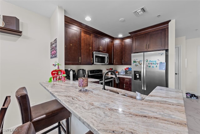 kitchen featuring a breakfast bar area, light stone countertops, sink, and appliances with stainless steel finishes