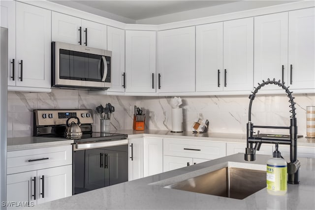 kitchen with backsplash, stainless steel appliances, white cabinetry, and sink