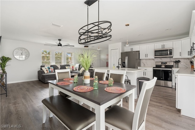 dining room with ceiling fan with notable chandelier, sink, and light hardwood / wood-style flooring