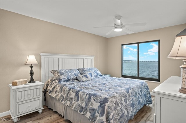 bedroom with light wood-type flooring, a water view, and ceiling fan