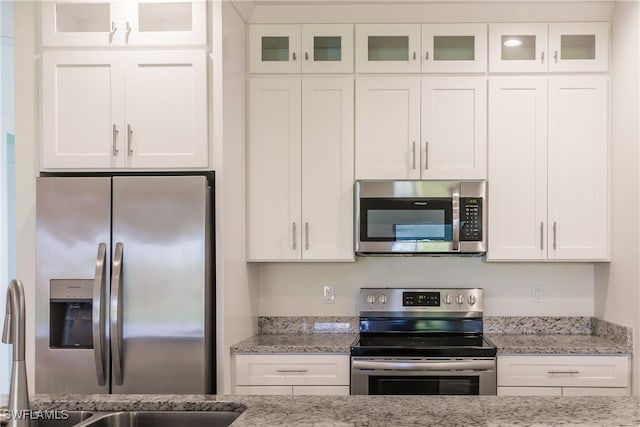 kitchen with white cabinets, appliances with stainless steel finishes, and light stone counters