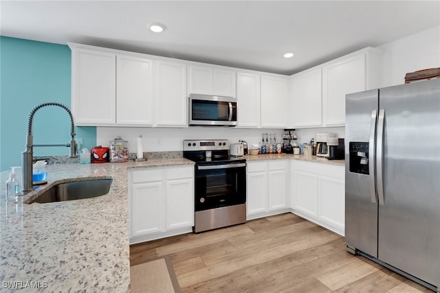 kitchen featuring light wood-type flooring, light stone counters, stainless steel appliances, sink, and white cabinets