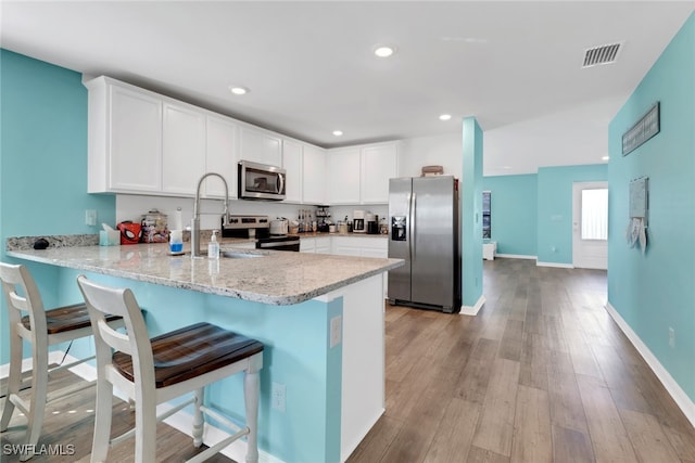 kitchen with kitchen peninsula, stainless steel appliances, light hardwood / wood-style flooring, white cabinetry, and a breakfast bar area