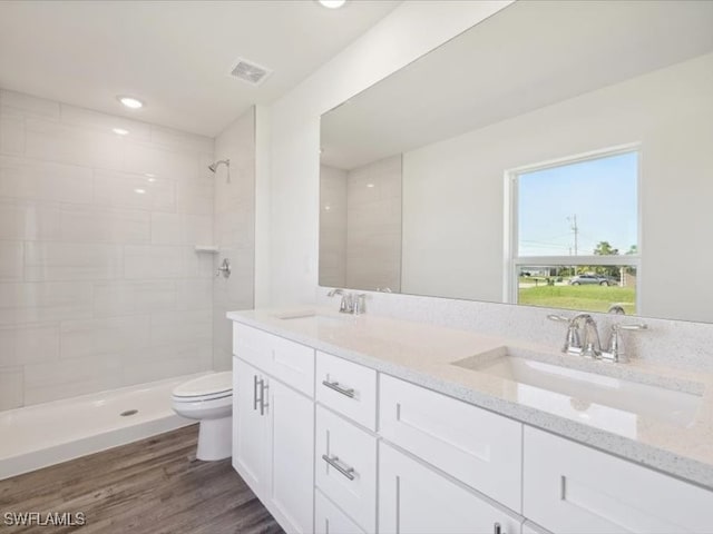 bathroom with hardwood / wood-style flooring, vanity, toilet, and a tile shower