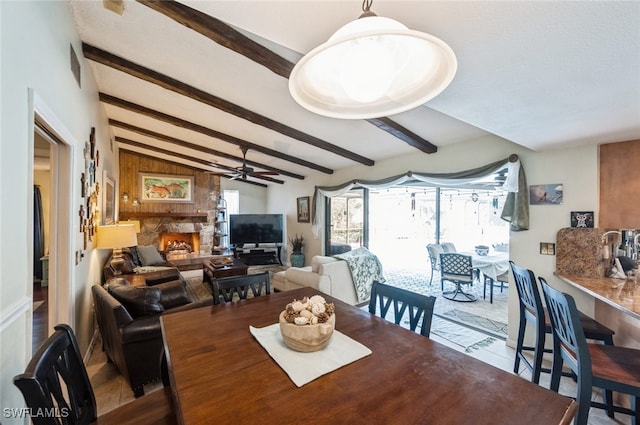 dining room with a stone fireplace, ceiling fan, and lofted ceiling with beams