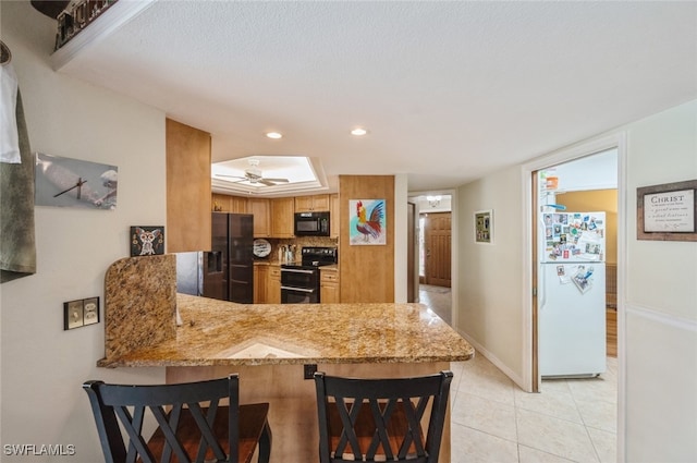 kitchen featuring black appliances, light tile patterned floors, light stone counters, kitchen peninsula, and a breakfast bar area