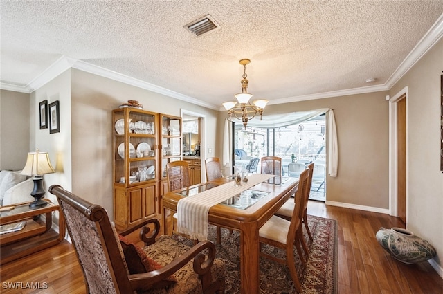 dining room featuring a textured ceiling, wood-type flooring, crown molding, and a chandelier