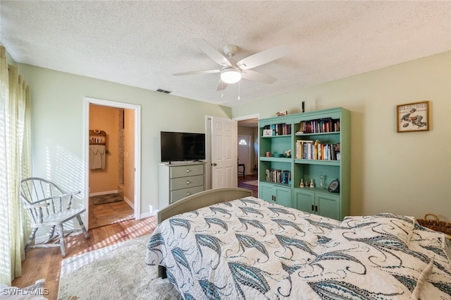 bedroom featuring hardwood / wood-style floors, ensuite bathroom, ceiling fan, and a textured ceiling