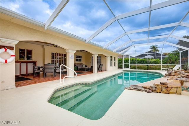 view of swimming pool with an outdoor living space, glass enclosure, ceiling fan, and a patio area