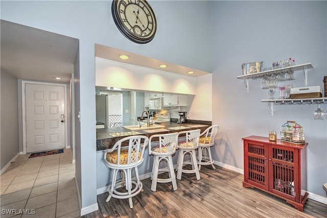 kitchen featuring stainless steel refrigerator, white cabinetry, sink, light hardwood / wood-style flooring, and decorative backsplash