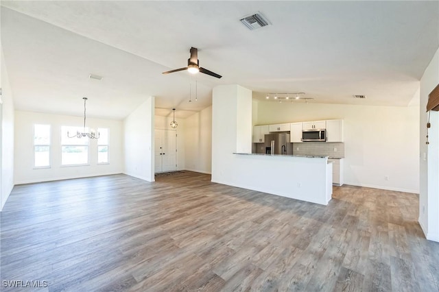 unfurnished living room with ceiling fan with notable chandelier, light hardwood / wood-style floors, and vaulted ceiling