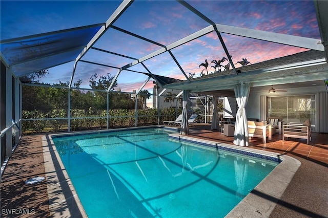 pool at dusk with glass enclosure, ceiling fan, and a patio area