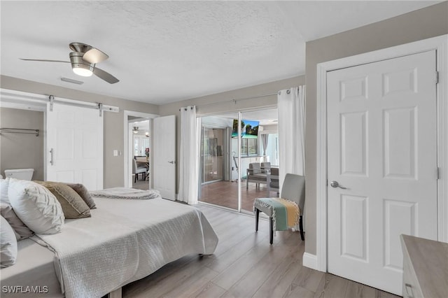 bedroom featuring a textured ceiling, ceiling fan, a barn door, light wood-style floors, and access to outside