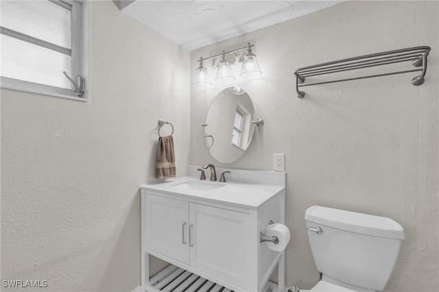 bathroom with a textured wall, vanity, and toilet