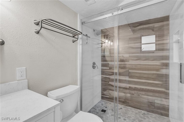 bathroom featuring a textured wall, a shower stall, toilet, and vanity