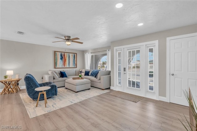 living area featuring a ceiling fan, light wood-type flooring, visible vents, and baseboards