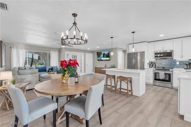 dining room with ceiling fan with notable chandelier and light hardwood / wood-style floors