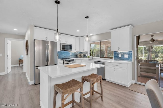 kitchen with light countertops, hanging light fixtures, appliances with stainless steel finishes, white cabinets, and a kitchen island