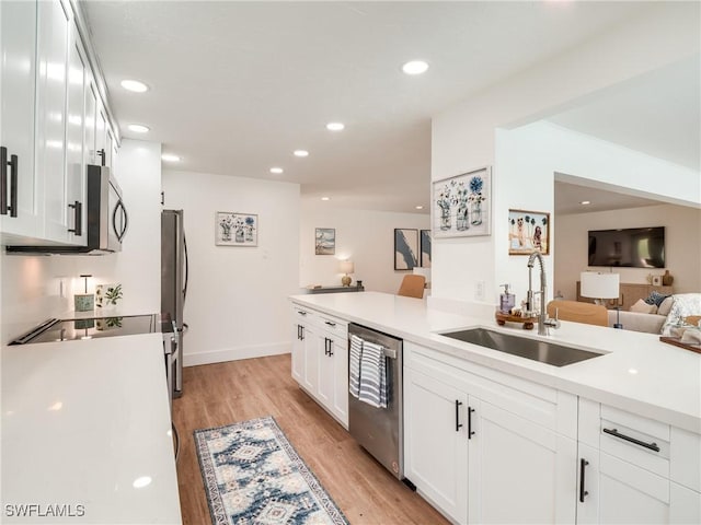 kitchen with kitchen peninsula, stainless steel appliances, sink, light hardwood / wood-style floors, and white cabinetry