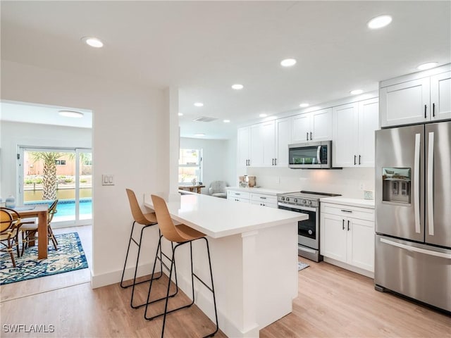 kitchen with white cabinets, appliances with stainless steel finishes, light hardwood / wood-style flooring, and a breakfast bar area