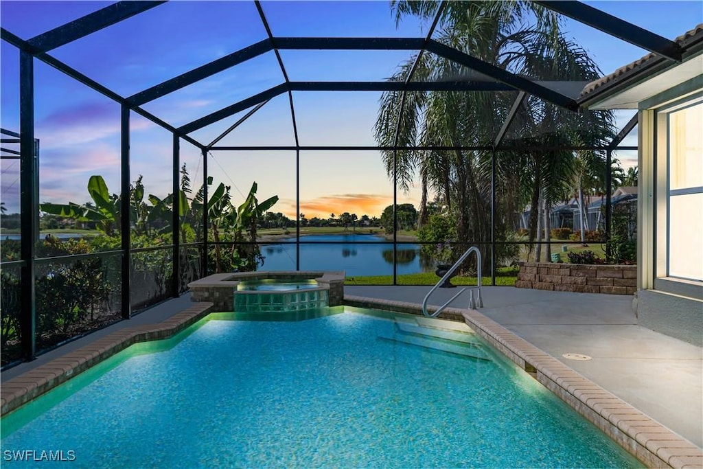 pool at dusk featuring an in ground hot tub, a patio, a water view, and glass enclosure