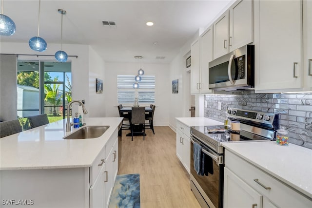 kitchen with a kitchen island with sink, sink, appliances with stainless steel finishes, decorative light fixtures, and white cabinetry