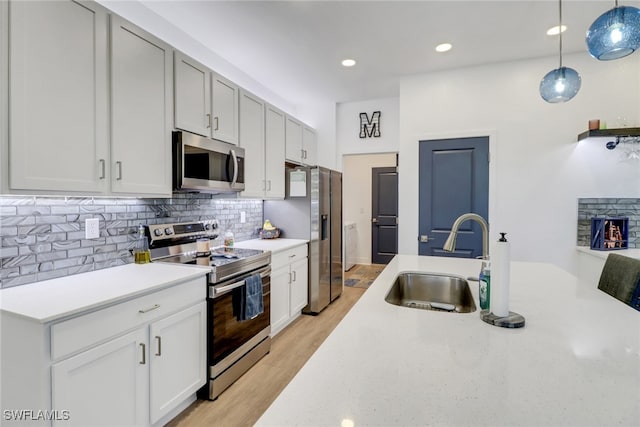 kitchen featuring sink, hanging light fixtures, stainless steel appliances, light hardwood / wood-style flooring, and white cabinets