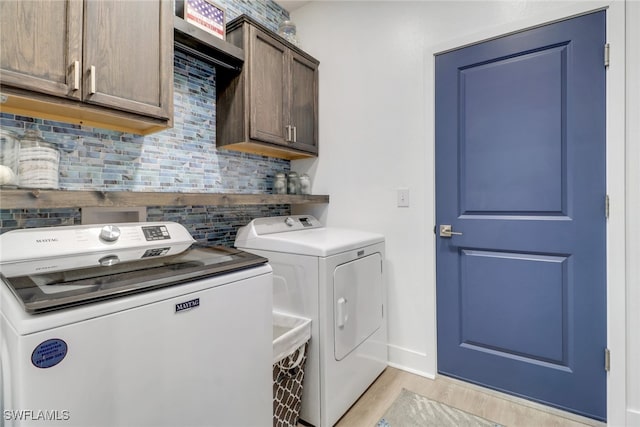 clothes washing area with washer and clothes dryer, cabinets, and light wood-type flooring