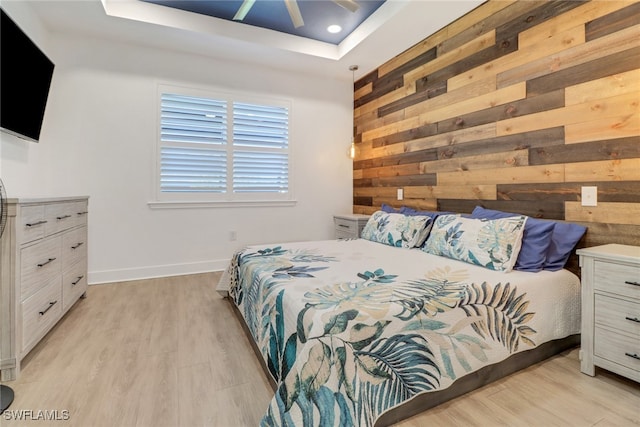 bedroom with a raised ceiling, wood walls, ceiling fan, and light wood-type flooring