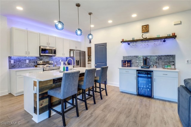 kitchen featuring white cabinets, hanging light fixtures, wine cooler, light hardwood / wood-style flooring, and stainless steel appliances