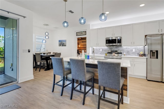 kitchen featuring a kitchen island with sink, light hardwood / wood-style flooring, decorative light fixtures, and appliances with stainless steel finishes