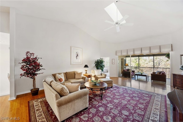 living room featuring a skylight, ceiling fan, high vaulted ceiling, and light wood-type flooring