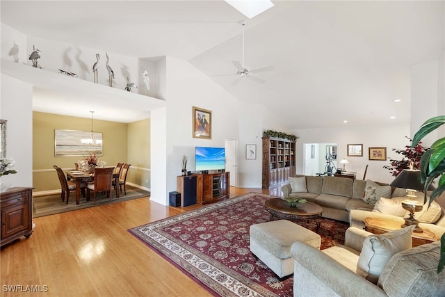 living room featuring wood-type flooring, ceiling fan with notable chandelier, a skylight, and high vaulted ceiling