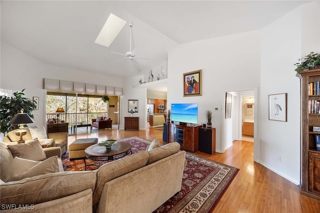 living room with ceiling fan, wood-type flooring, high vaulted ceiling, and a skylight