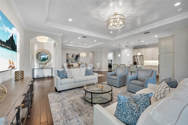 living room with an inviting chandelier, hardwood / wood-style floors, a tray ceiling, ornamental molding, and washer / dryer