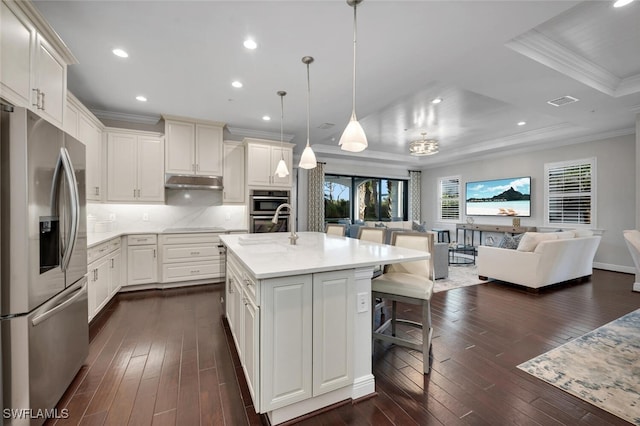 kitchen featuring a breakfast bar area, appliances with stainless steel finishes, a kitchen island with sink, white cabinets, and decorative light fixtures