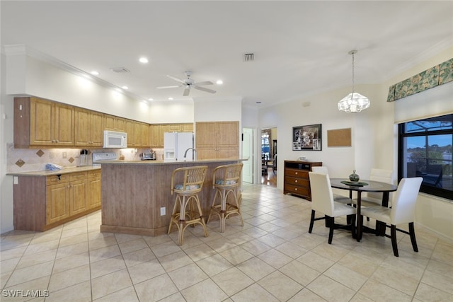 kitchen with pendant lighting, crown molding, white appliances, and a kitchen island with sink