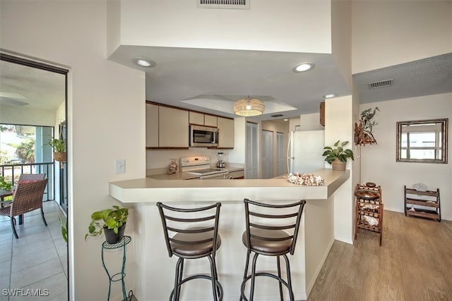 kitchen with white appliances, cream cabinets, a kitchen breakfast bar, light hardwood / wood-style floors, and kitchen peninsula