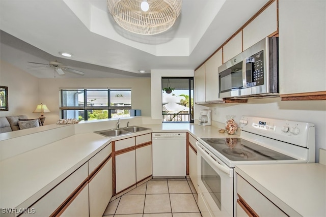 kitchen with white appliances, a tray ceiling, sink, light tile patterned floors, and white cabinets