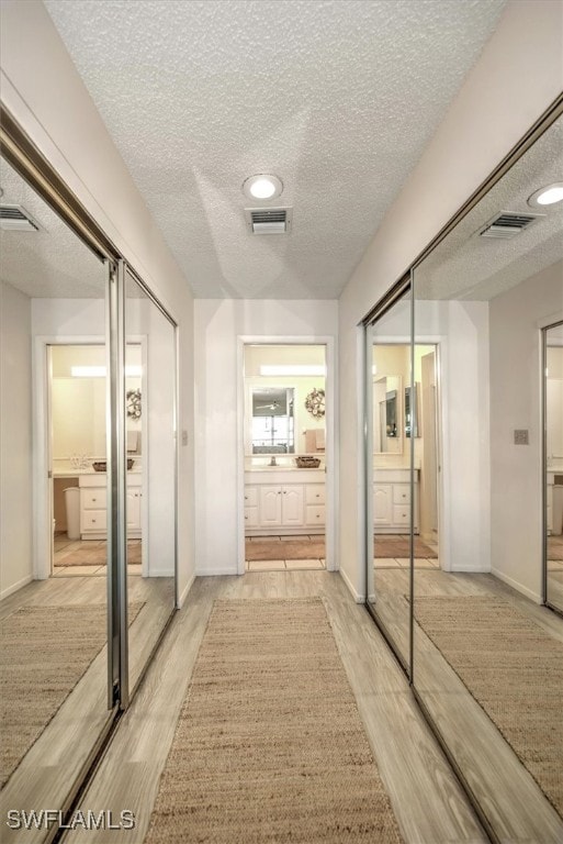 corridor with a textured ceiling and light wood-type flooring