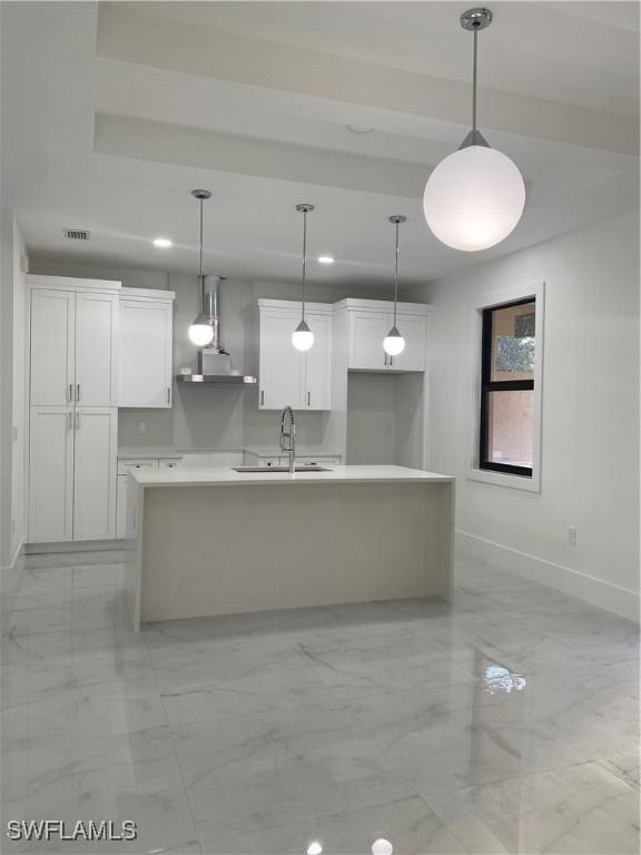 kitchen with a center island with sink, pendant lighting, white cabinetry, and sink