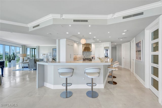 kitchen featuring a large island, wall chimney exhaust hood, a kitchen bar, and crown molding