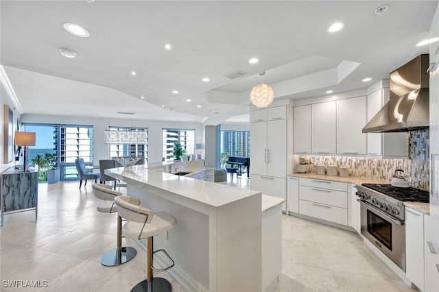 kitchen with a healthy amount of sunlight, a center island with sink, white cabinetry, and wall chimney exhaust hood