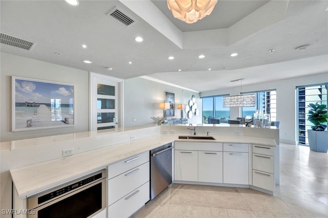 kitchen featuring kitchen peninsula, appliances with stainless steel finishes, sink, pendant lighting, and white cabinetry