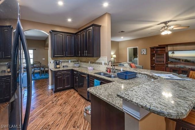 kitchen with dark brown cabinets, light wood-type flooring, light stone counters, sink, and kitchen peninsula